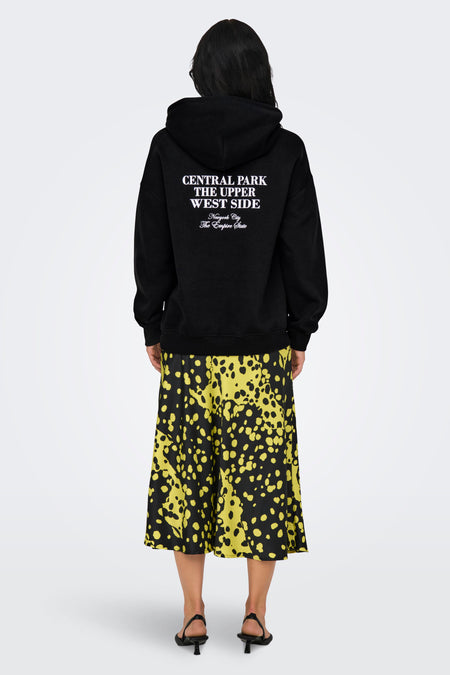 Zwarte sweater met kap van ONLY, met tekstprint op de rug, gecombineerd met een geel en zwart geprinte rok.
