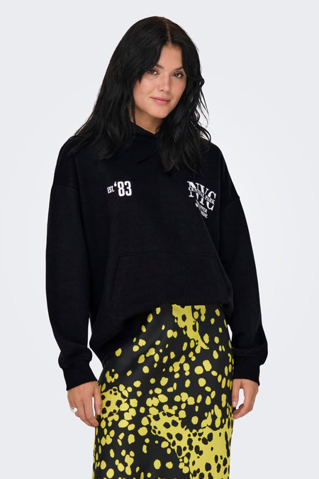 Pull-over noir avec capuche ONLY, imprimé de "NYC" et "Est. '83" en blanc, associé à une jupe jaune à carreaux.