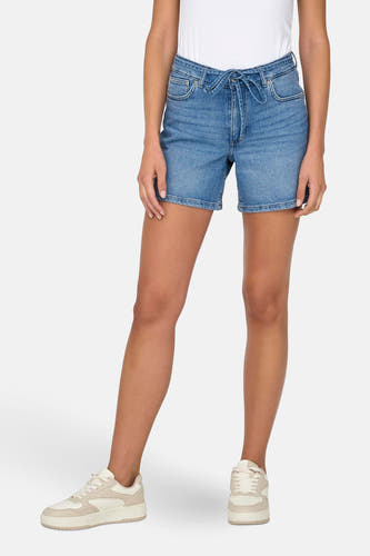 Korte mid blue denim short van ONLY, met een strikceintuur en gecombineerd met witte sneakers.
