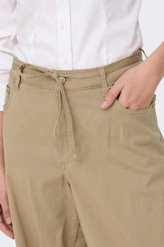 Beige broek van ONLY met een strikceintuur en een hand in de zak.
