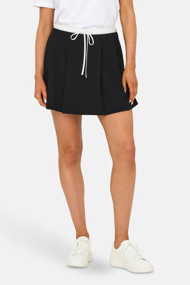 Zwarte korte rok van ONLY, met witte trekkoordsluiting en gedragen met witte sneakers en een wit shirt.
