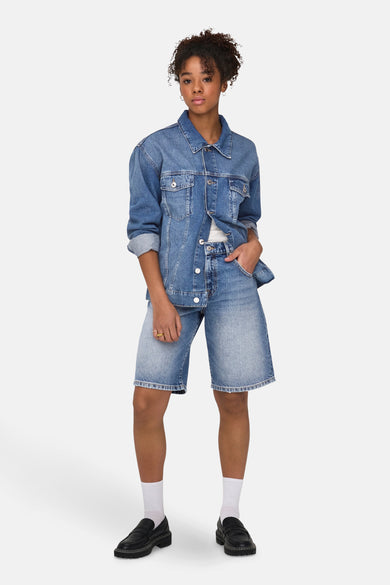Middenblauwe denim short van ONLY, gecombineerd met een denim jack, witte sokken en zwarte loafers.
