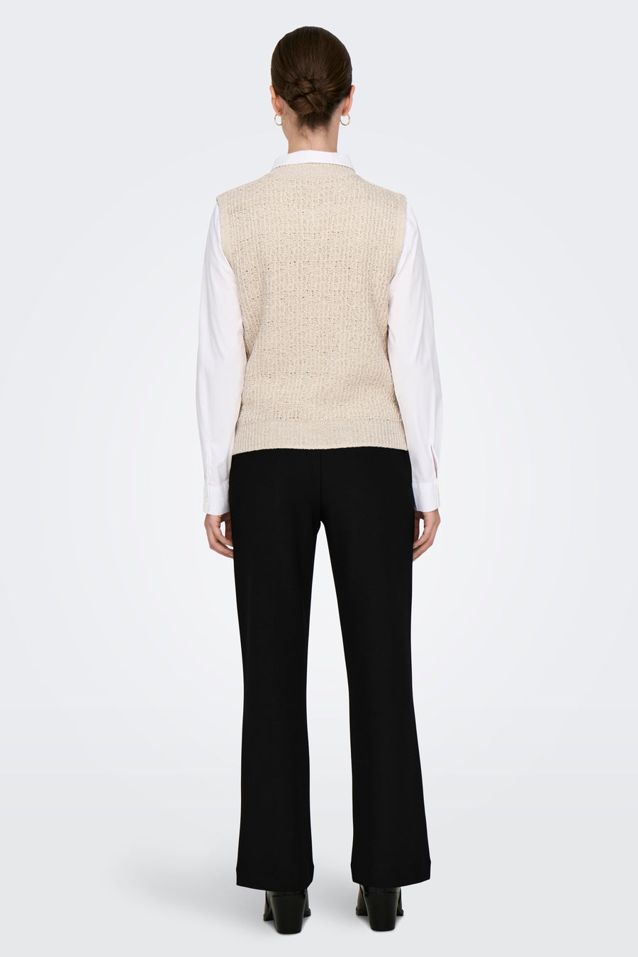Ecrukleurig gilet van ONLY, rugaanzicht, gedragen over een wit overhemd met zwarte broek en hakken.
