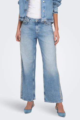 Jean en denim bleu clair large de ONLY, avec des franges argentées le long du côté, associé à un blouson en cuir et des escarpins bleus.