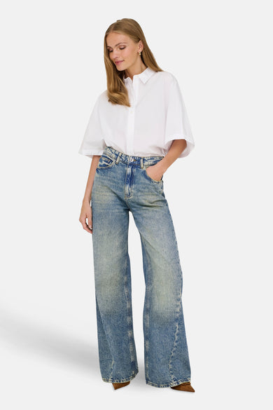 Wijde jeans van blauw denim van JDY, gedragen met een wit overhemd en bruine schoenen.

