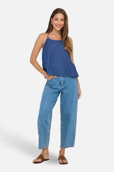 Mouwloze blauwe denim blouse van ONLY, met spaghettibandjes, gecombineerd met wijde jeans en bruine sandalen.
