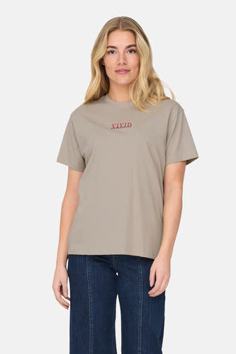 Beige T-shirt met korte mouwen van ONLY, met rode tekstprint, gecombineerd met een donkerblauwe broek.
