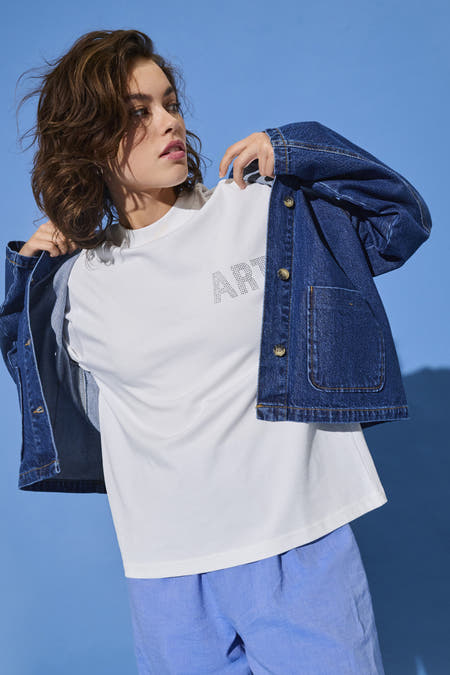 Wit T-shirt met korte mouwen van ONLY, met stippenpatroon dat het woord "ART" vormt, gecombineerd met een spijkerjack en blauwe linnen shorts.