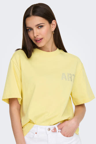 T-shirt jaune à manches courtes de ONLY, avec des strass, porté avec un pantalon blanc.
