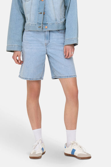 Lichtblauwe denim short van ONLY, gecombineerd met een jeans jack en witte sportschoenen met blauwe details.
