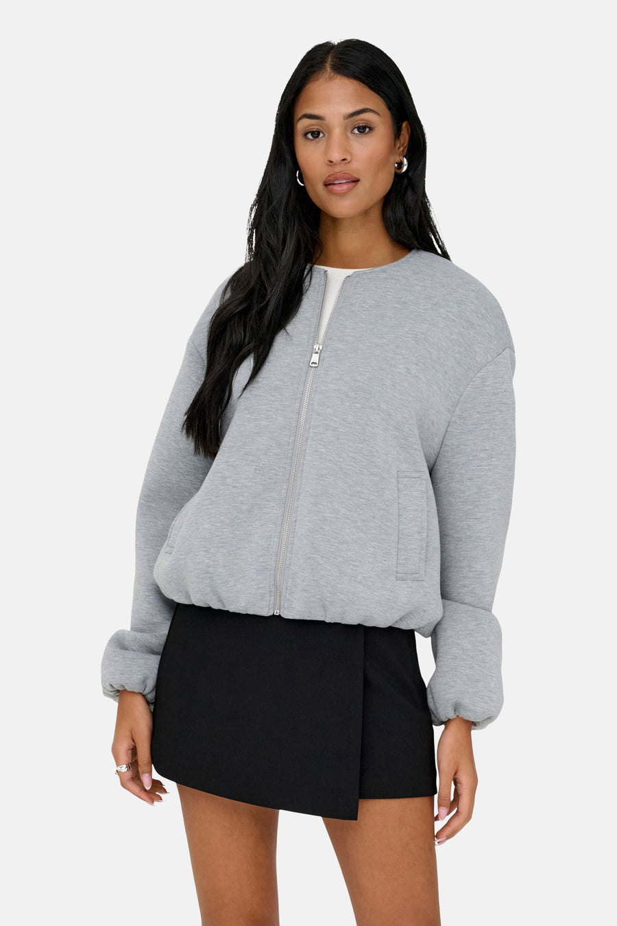 Veste courte grise de ONLY® avec fermeture éclair, poches plaquées et manches retroussées, portée avec une mini-jupe noire.