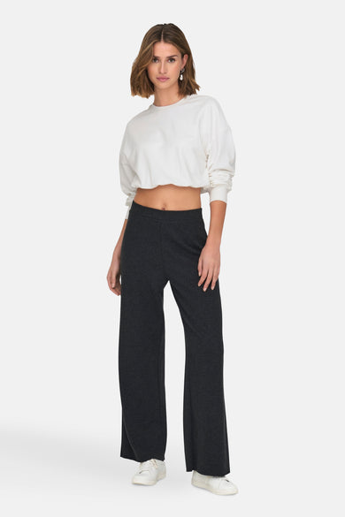 Witte sweater van ONLY®, gedragen met wijde, donkergrijze broek en witte sneakers.