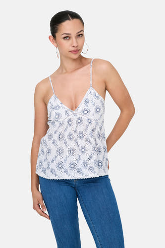 Witte blouse zonder mouwen van ONLY, met blauw bloemenpatroon, gedragen met een blauwe jeans en gouden oorbellen.
