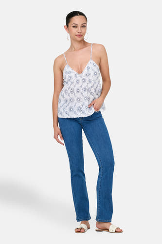 Witte mouwloze blouse van ONLY®, met een bloemenpatroon, gecombineerd met blauwe jeans en witte sandalen.
