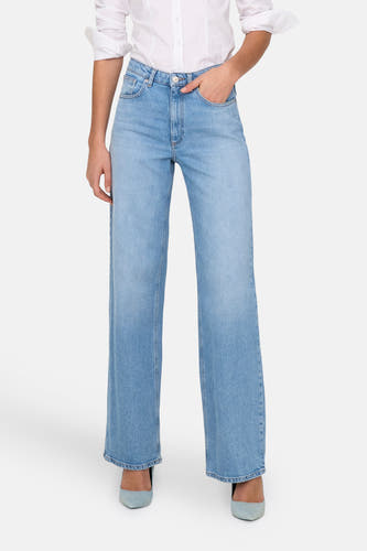 Lichtblauwe, wijde jeans van ONLY, met een hand in de zak en gecombineerd met een wit overhemd en blauwe schoenen.
