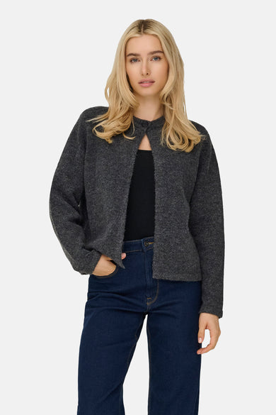 Vrouw met blond haar, grijze cardigan en blauwe jeans.