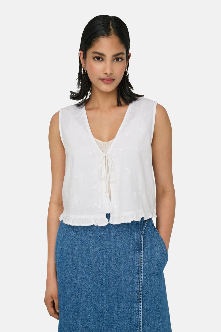 Witte mouwloze blouse van ONLY, met geborduurde details en een geplooide zoom, gecombineerd met een blauwe rok.
