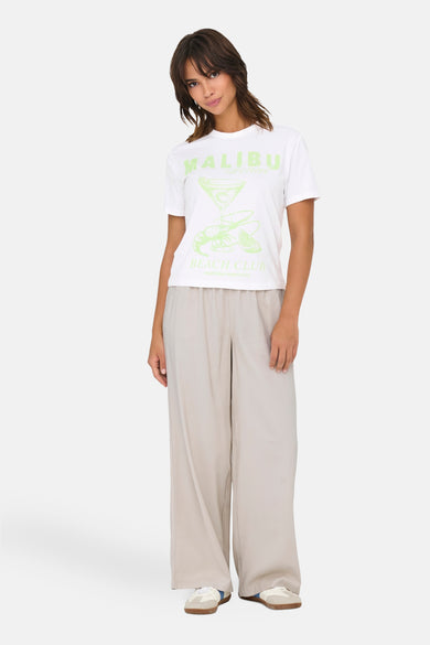 Wit T-shirt met korte mouwen van ONLY, met lichtgroene "Malibu Beach Club" print, gecombineerd met een beige broek en sneakers.
