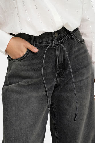 Donkergrijze rechte jeans van ONLY, met strikceintuur en een hand in de zak, gecombineerd met een wit, glanzend overhemd.
