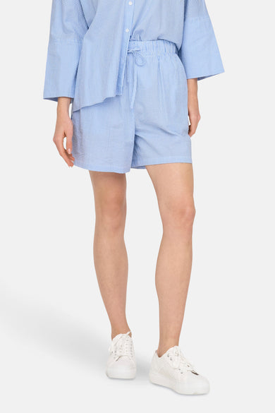 Blauwe short van ONLY®, met witte strepen, gecombineerd met een gestreept overhemd en witte sneakers.
