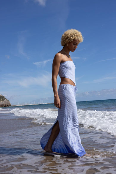 Lange blauwe rok van ONLY, met witte strepen en een split, gedragen door een model op het strand.

