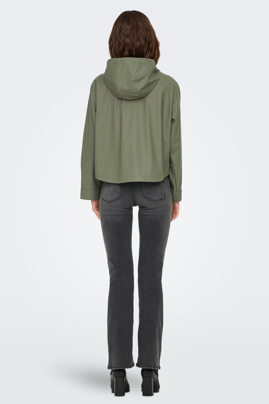 Kaki regenjas van ONLY, met een capuchon, gecombineerd met een grijze jeans en zwarte laarzen.