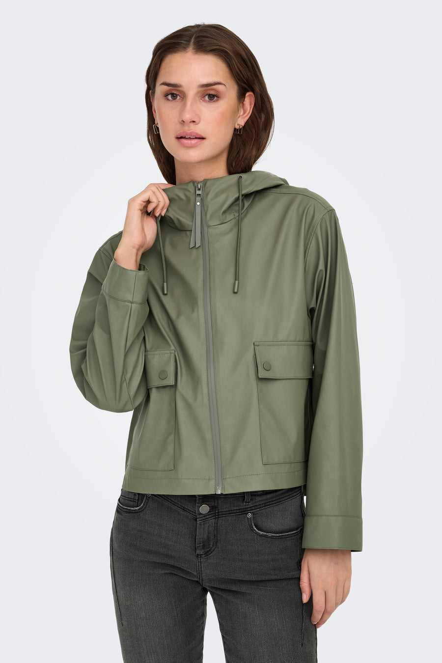 Kakikleurige regenjas van ONLY, met capuchon, zakken met knoopsluiting en gedragen over een donkere jeans.
