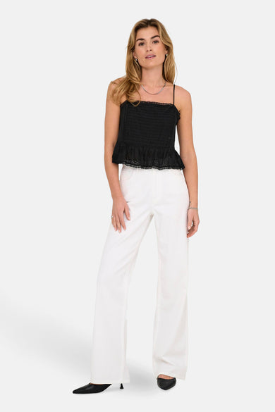 Blouse noire sans manches de ONLY, avec des détails brodés en bas, associée à un pantalon blanc et des baskets noires.