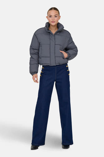 Grijze korte jas van ONLY, gedragen met donkerblauwe jeans met knoopdetails en zwarte schoenen.