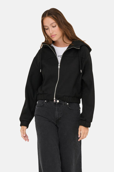 Zwarte korte jas van ONLY, met capuchon en zilverkleurige ritssluiting, gedragen met een witte top en zwarte jeans.
