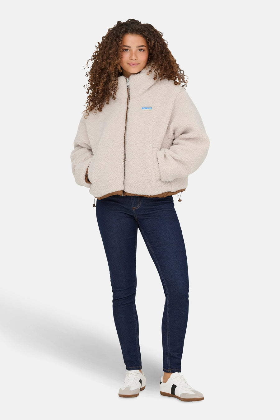 Ecru korte jas van ONLY, met bruine details en gedragen met een donkere jeans en witte sneakers.
