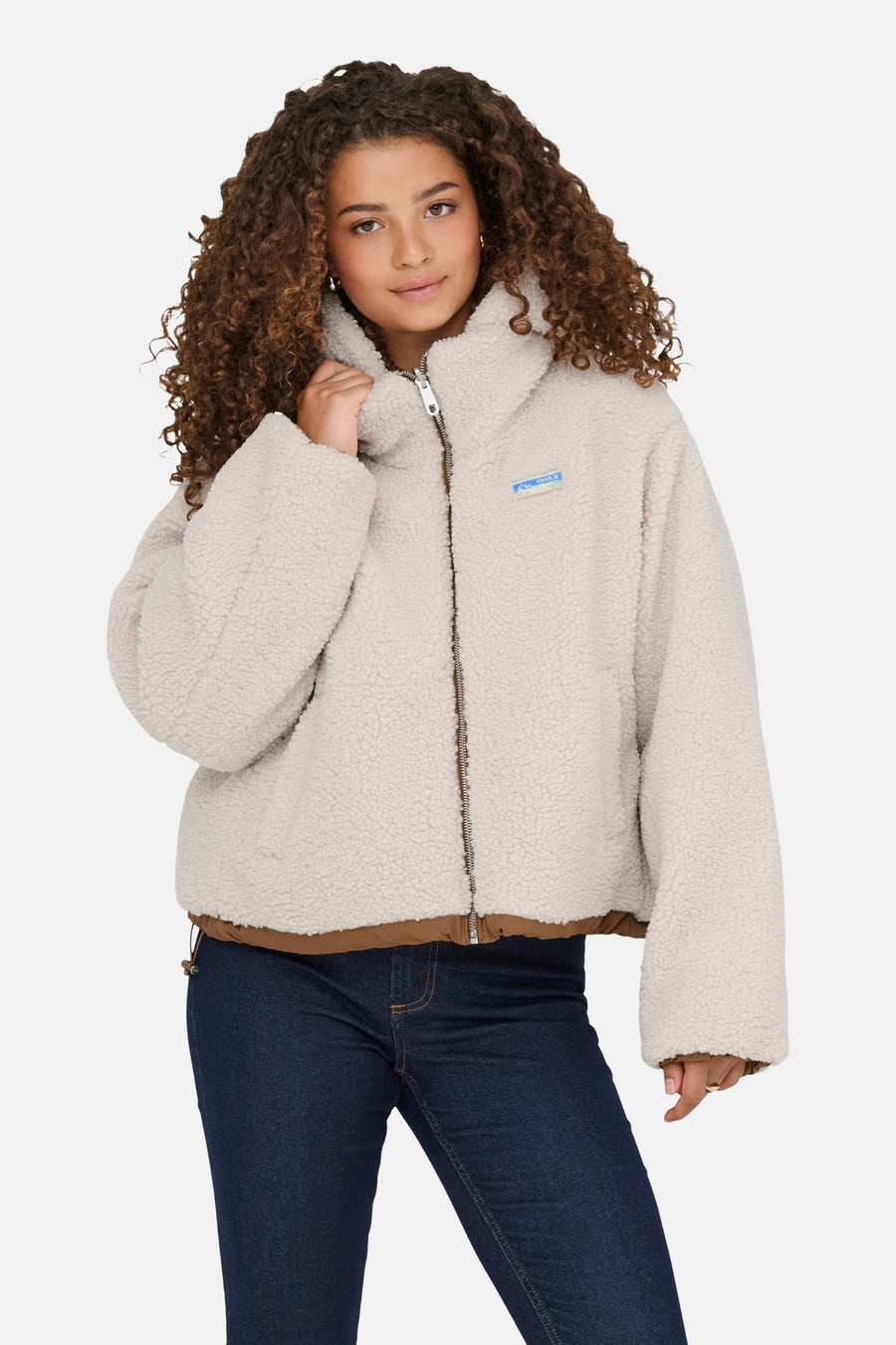 Ecru korte jas van ONLY, met ritssluiting en donkerblauwe jeans.
