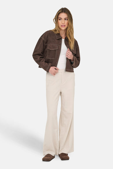 Bruine korte jas van ONLY®, met contrasterende stiksels en gedragen over een wit shirt en beige broek.
