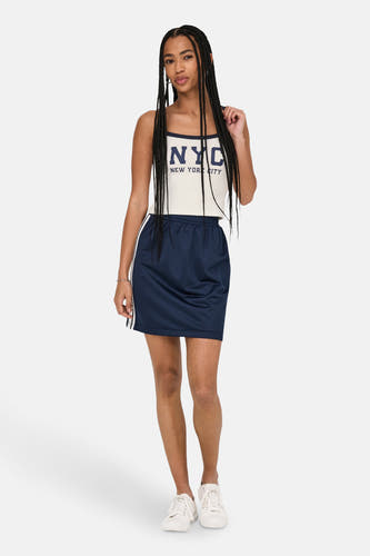 Witte top van ONLY®, met een donkerblauwe NYC print en gedragen met een marineblauwe rok en witte sneakers.

