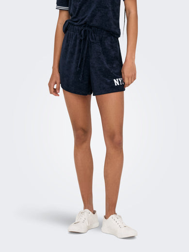 Blauwe short van ONLY, met trekkoord en witte "NYC" letters op de voorkant, gedragen met witte schoenen.
