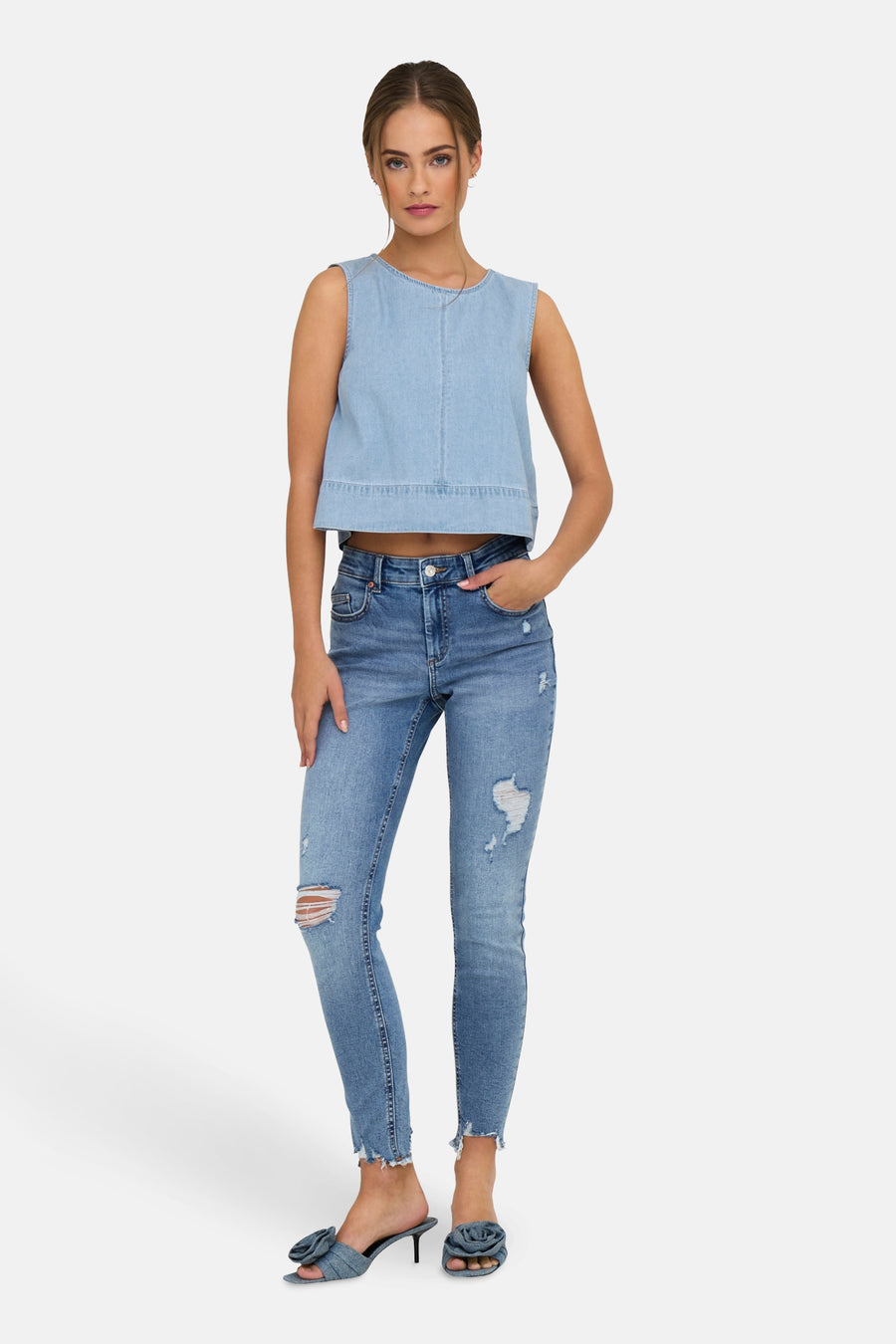 Vrouw in blauwe denim top en gescheurde jeans, staand.