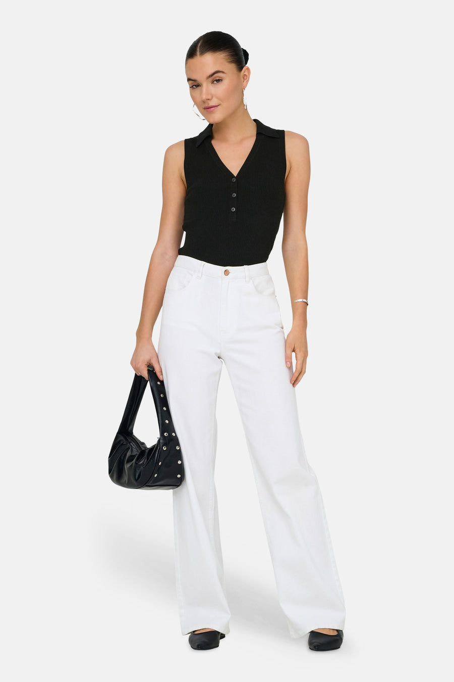 Haut noir sans manches de JDY, avec fermeture à boutons et porté avec un pantalon blanc et un sac noir.