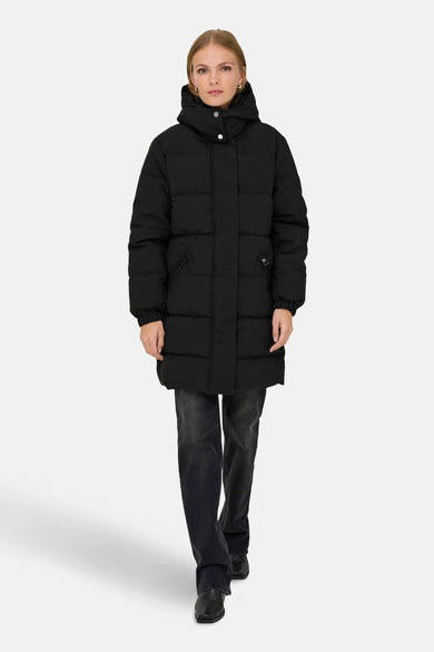 Manteau long noir de JDY, avec capuche et porté sur des jeans noirs et des bottes noires.