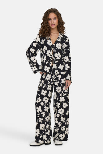 Zwarte blouse met lange mouwen van JDY, met een bloemenpatroon, gecombineerd met een bijpassende broek en witte schoenen.
