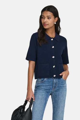 Blauw gilet van JDY, met zilveren knopen en korte mouwen, gedragen met een blauwe jeans en zwarte handtas.
