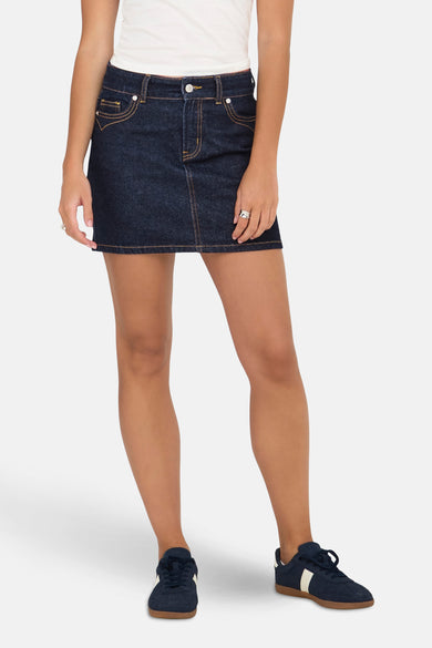 Korte rok van donkerblauw denim van ONLY, met geel stiksel en gecombineerd met een wit topje en blauwe sneakers.
