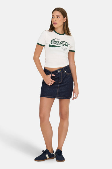 Donkerblauwe, denim korte rok van ONLY, gecombineerd met een wit T-shirt met logo en blauwe sneakers.
