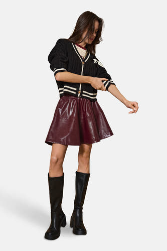 Cardigan noir d'ONLY, avec des rayures blanches et porté avec une jupe rouge et des bottes noires.