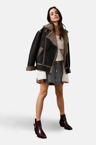 Korte donkerblauwe denim jas van ONLY, met bruine accenten en een wollige kraag, gecombineerd met een rok en enkellaarsjes.
