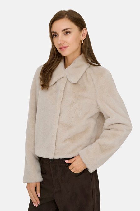 Lichtgrijze bontjas met opstaande kraag van JDY, zachte textuur, model in zijprofiel, donkere broek, hand in zak