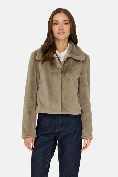 Beige korte jas van JDY, gedragen over een wit overhemd en een donkere spijkerbroek.
