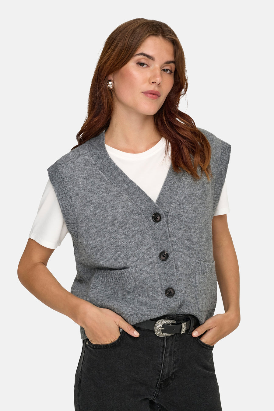 Grijs debardeur van JDY, met knoopsluiting en zakken, gedragen over een wit T-shirt en zwarte jeans met riem.
