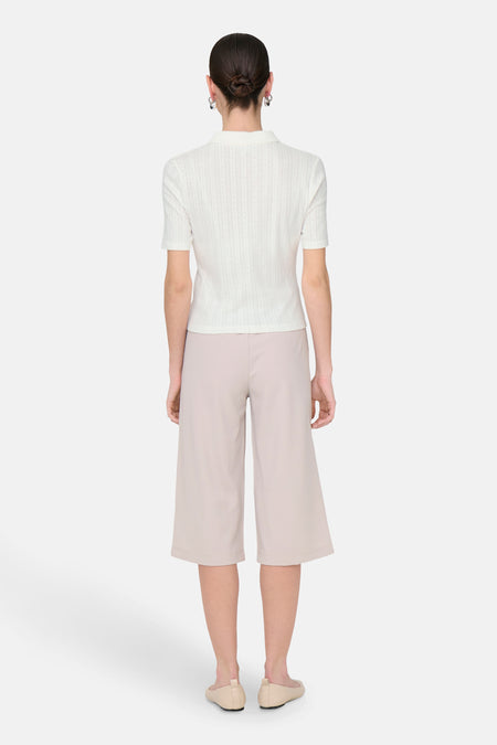 Witte polo met korte mouwen van JDY, met een subtiel structuurpatroon en gecombineerd met beige culottes en ballerina's.
