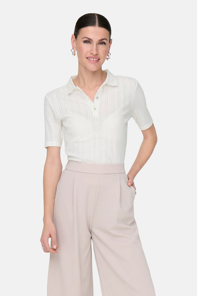Witte polo met korte mouwen van JDY, met fijn structuurdessin, gedragen met wijde, beige pantalon.
