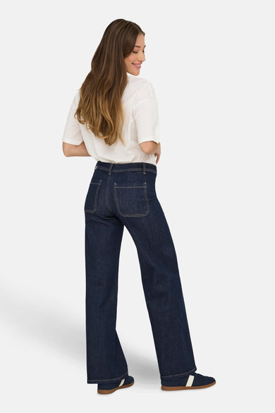 Jeans straight van donkerblauw denim van JDY, gezien van achteren, met wit shirt en blauwe sneakers.